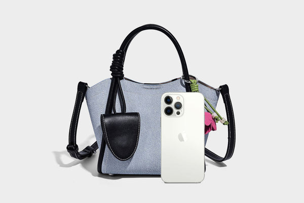 Light blue denim trapezoid tote bag with black leather-look trim, knotted top handles, detachable crossbody strap, front