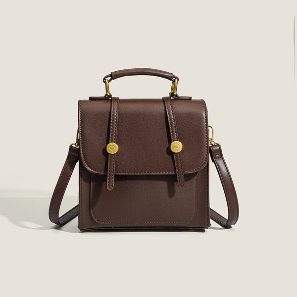 Structured mini satchel backpack with smooth leather-look finish, front flap pocket, gold-tone stud closures, and top handle