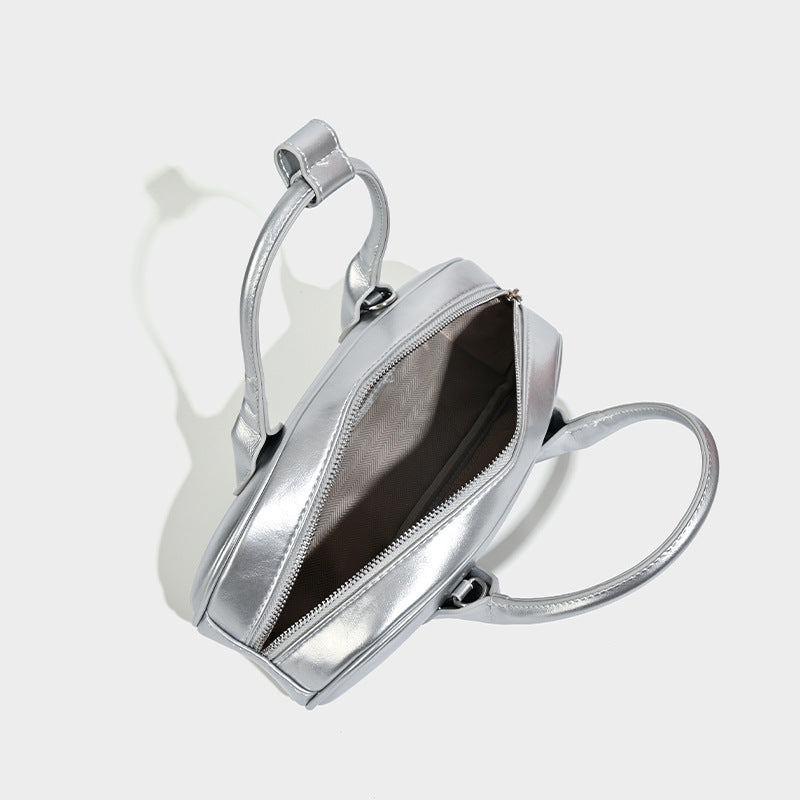 Kompakte silberfarbene Mini-Boston-Tasche mit zwei Tragegriffen oben, silberfarbenen Metallelementen und abnehmbarem Crossbody-Riemen, Detailansicht