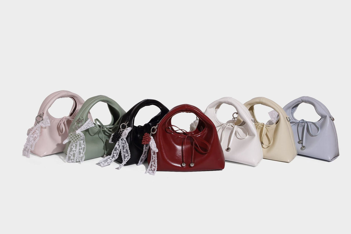 Kleine kuppelförmige Henkeltasche in glänzender Lederoptik mit Kordelzugverschluss, weißem Spitzen-Schleifenanhänger und silberfarbenen Metallbeschlägen
