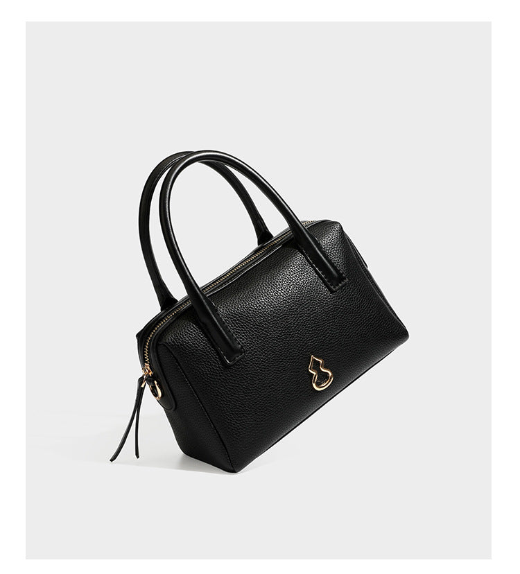 Small structured pillow satchel bag with pebbled leather-look finish, dual rolled top handles, gold-tone gourd emblem, and