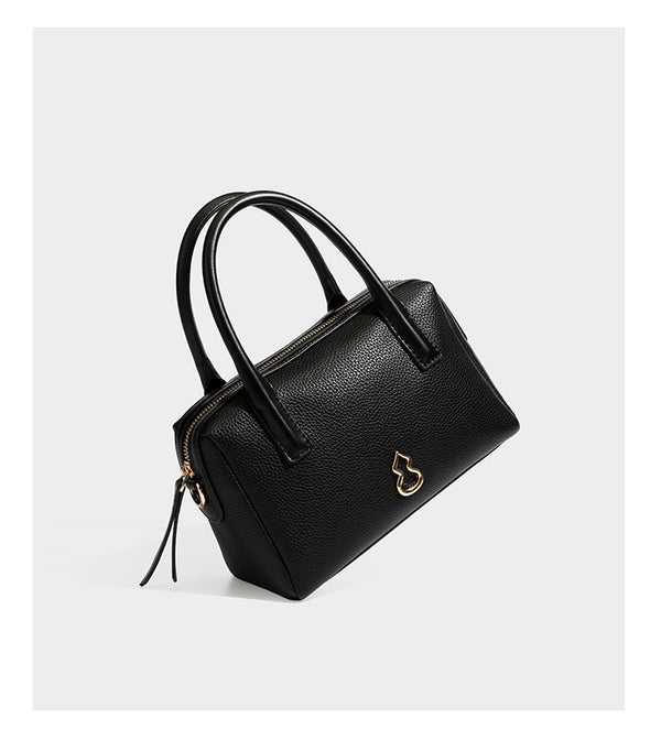 Small structured pillow satchel bag with pebbled leather-look finish, dual rolled top handles, gold-tone gourd emblem, and