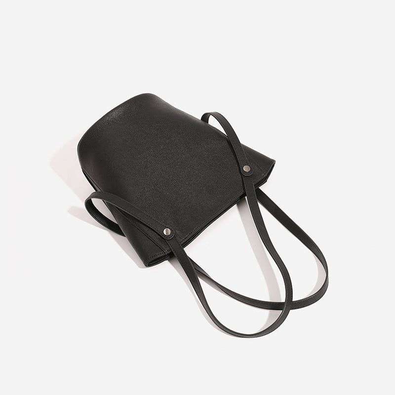 Structured black leather-look bucket tote bag with slim shoulder straps, silver-tone stud hardware, and tapered body, detail