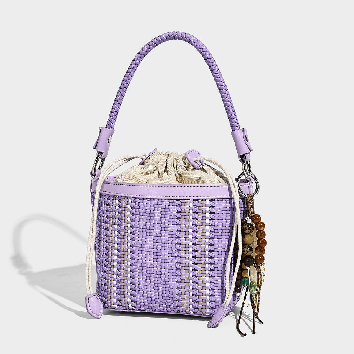 Small woven bucket bag with drawstring top, braided handle, detachable crossbody strap, and silver-tone ring hardware, detail