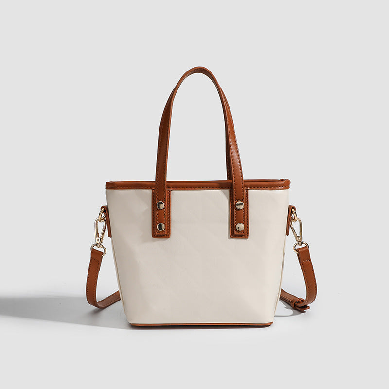 Kleine strukturierte Tote-Bag mit hellbraunen Henkeln und Besatz im Lederlook auf cremefarbenem Korpus, Reißverschluss oben, goldfarbenen Nieten und Vorderansicht