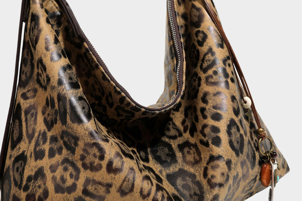 Slouchy leopard print hobo shoulder bag with glossy coated finish, top zipper closure, dark brown trim, and dangling charm