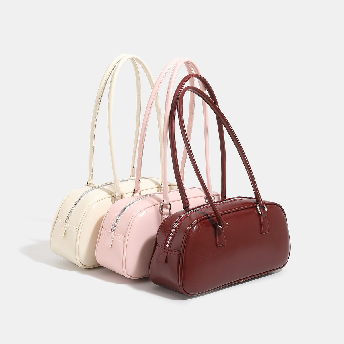 Rounded baguette shoulder bag with glossy leather-look finish, double-pull zip top, dual top handles, and silver-tone, detail
