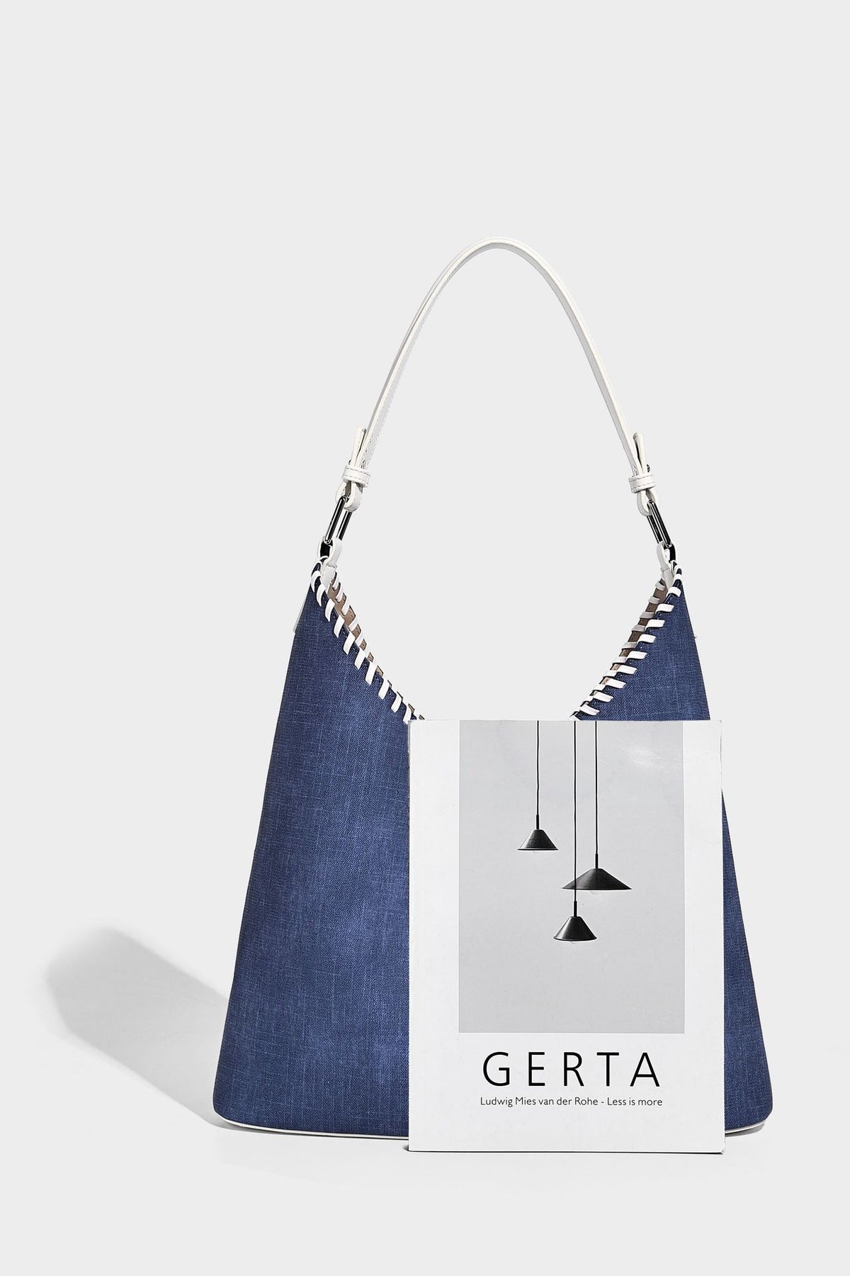 Denim-blue hobo tote with white leather-look shoulder strap, contrast whipstitch trim along curved open top, and silver-tone