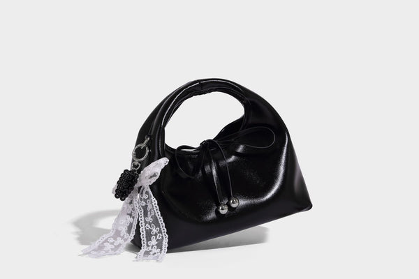Kleine kuppelförmige Henkeltasche in glänzender Lederoptik mit Kordelzugverschluss, weißem Spitzen-Schleifenanhänger und silberfarbenen Metallbeschlägen
