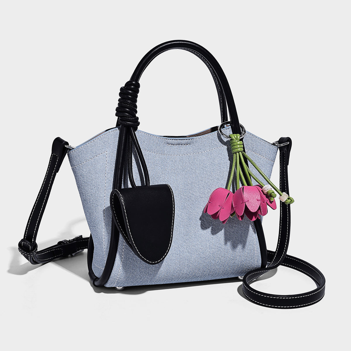Light blue denim trapezoid tote bag with black leather-look trim, knotted top handles, detachable crossbody strap, front