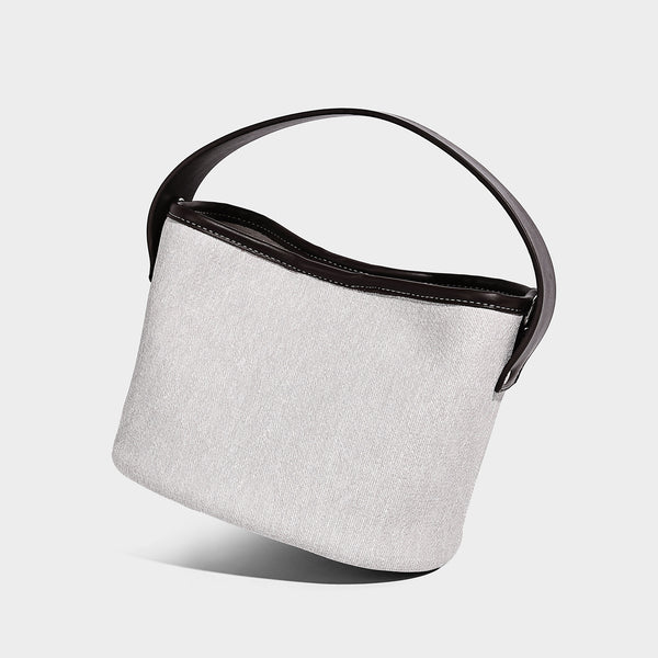 Small denim-look bucket bag with black leather-look trim, pink tulip flower charm, and adjustable crossbody strap, front view