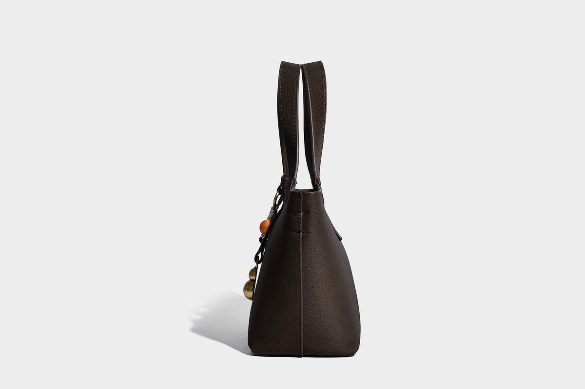 Kleine matte Beuteltasche mit genarbter Oberfläche, antikgoldfarbenen Ringbeschlägen, Perlen- und Quastenanhänger, kurzen Tragegriffen oben und