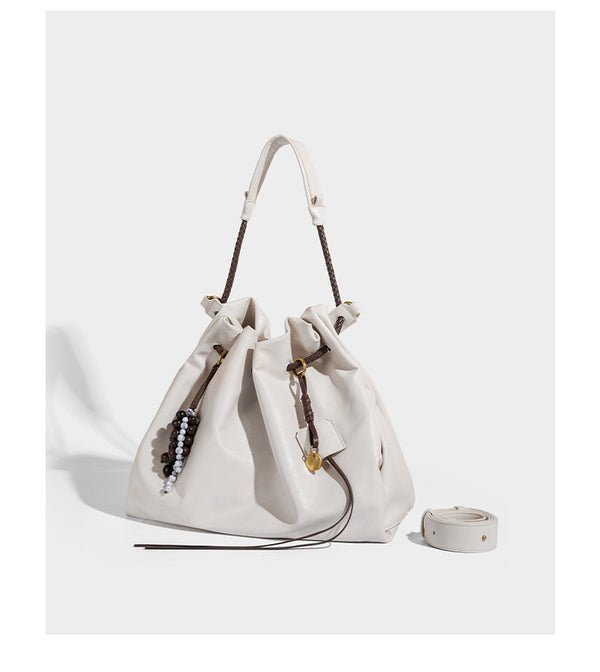 Cream slouchy drawstring bucket bag with braided cord, beaded tassel charm, and gold-tone ring hardware, detail view 8