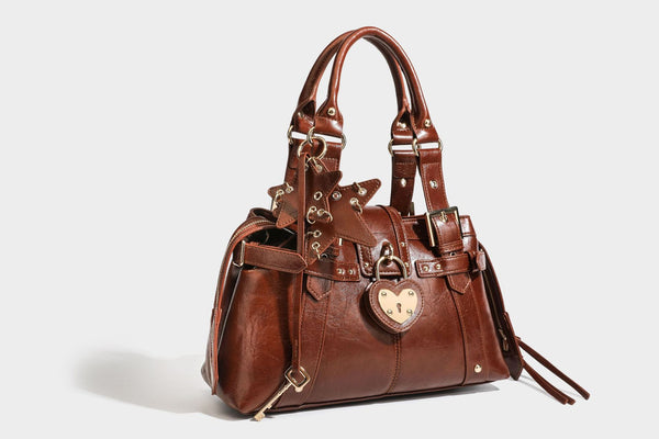 Structured leather-look satchel bag with heart padlock charm, star charm, gold-tone buckle hardware, dual top handles, and
