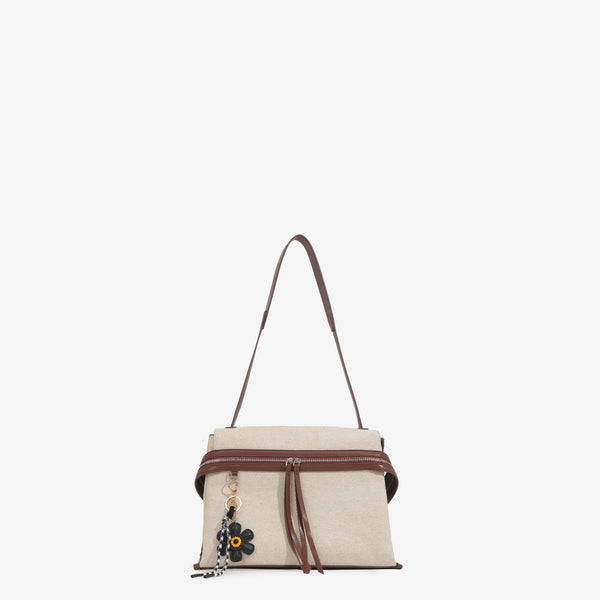 Cream canvas tote bag with brown leather-look trim, dual exterior zip pockets, long shoulder strap, and black flower charm
