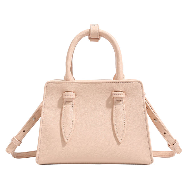 Small structured trapezoid top-handle bag in pebbled matte finish with decorative strap tabs, twin knotted handles, and