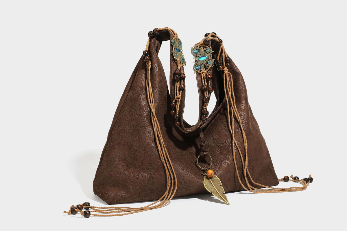 Slouchy boho hobo shoulder bag in embossed brown suede-look finish with beaded strap, cord tassels, and brass-tone leaf