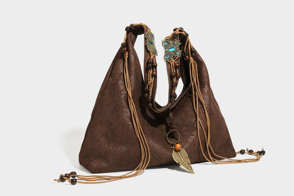 Slouchy boho hobo shoulder bag in embossed brown suede-look finish with beaded strap, cord tassels, and brass-tone leaf