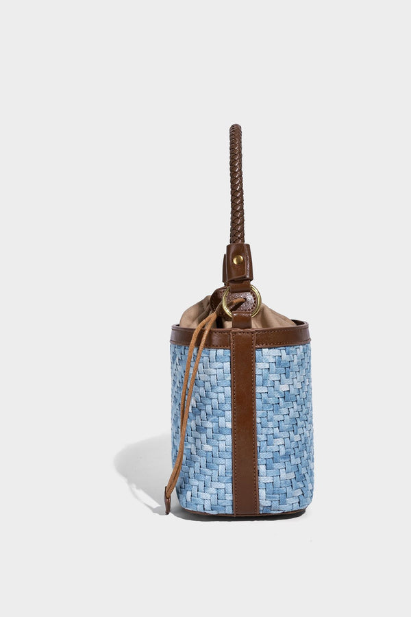 Small light blue woven bucket bag with brown leather-look trim, braided top handle, brass-tone ring hardware, drawstring