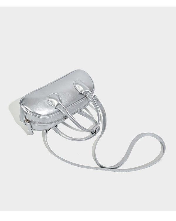 Kompakte Mini-Boston-Tasche in Silbermetallic mit zwei Tragegriffen oben, silberfarbenen Beschlägen und abnehmbarem Crossbody-Riemen, Detailansicht
