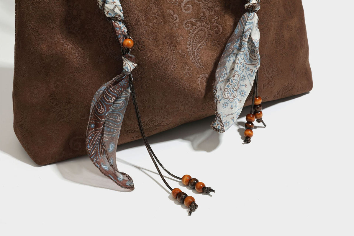 Slouchy paisley-embossed suede-look shoulder tote bag with braided patterned fabric straps and wood bead accents, detail view