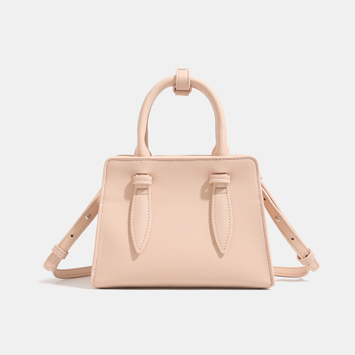 Small structured trapezoid top-handle bag in pebbled matte finish with decorative strap tabs, twin knotted handles, and