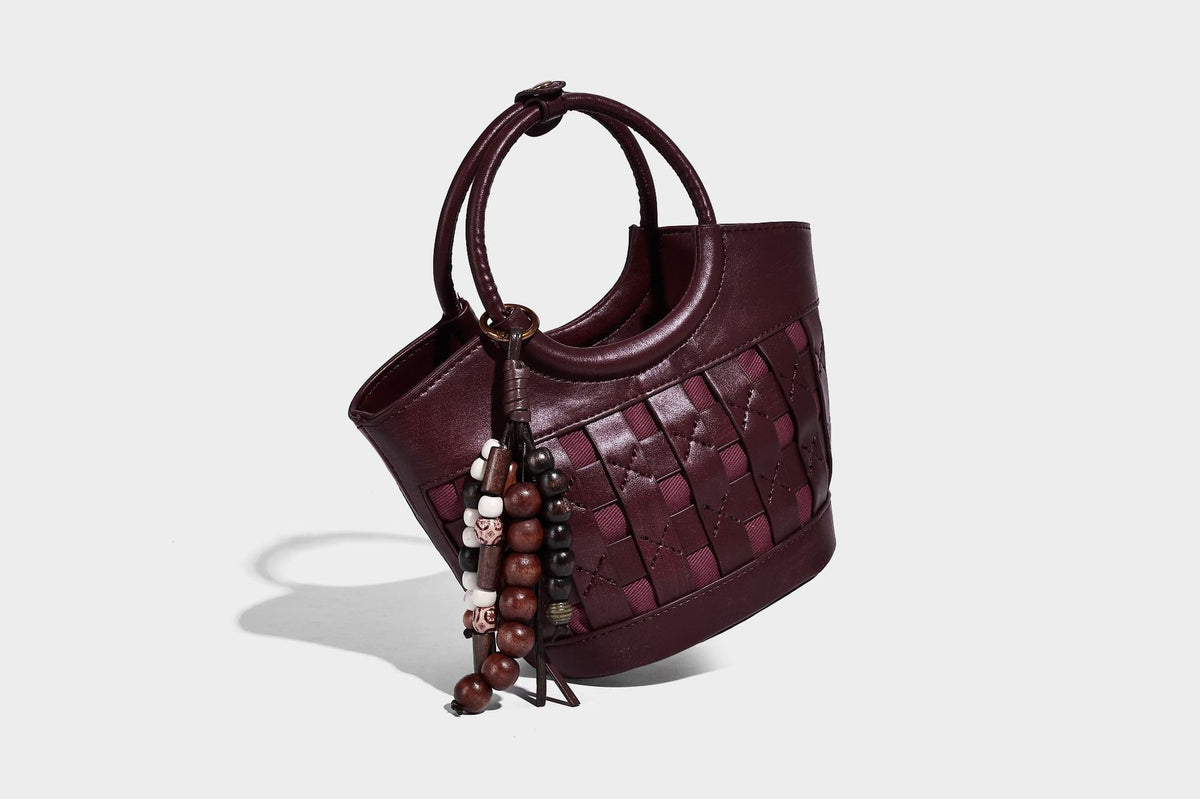 Small woven-panel bucket bag with circular ring handles, beaded tassel charm, and detachable crossbody strap in brown, detail