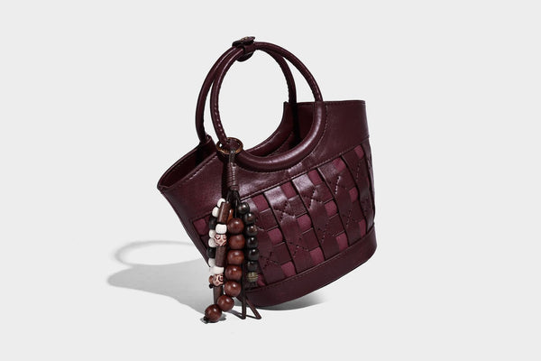 Small woven-panel bucket bag with circular ring handles, beaded tassel charm, and detachable crossbody strap in brown, detail