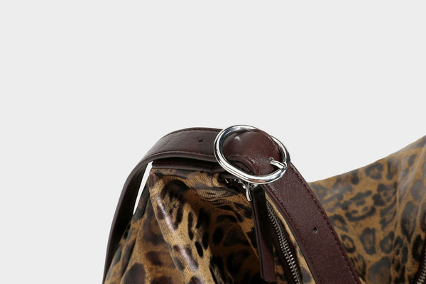 Slouchy leopard print hobo shoulder bag with glossy coated finish, top zipper closure, dark brown trim, and dangling charm