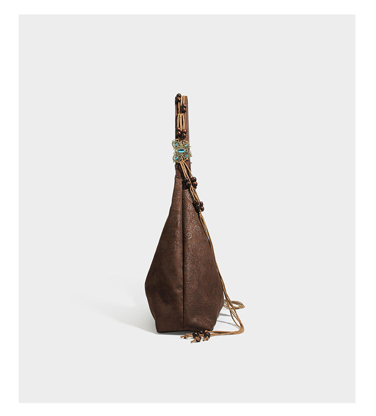Slouchy boho hobo shoulder bag in embossed brown suede-look finish with beaded strap, cord tassels, and brass-tone leaf