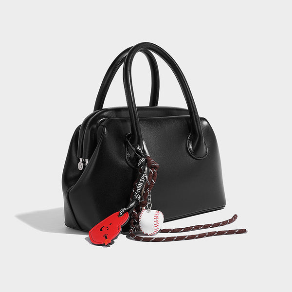 Small structured shell top-handle bag in red with heart charm and braided cord detail, smooth leather-look finish, detail