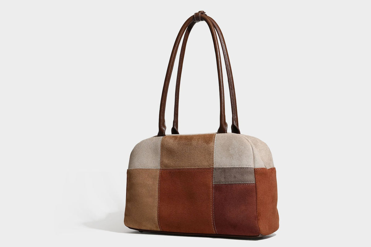 Boxy patchwork suede-look shoulder tote in tan, beige, rust, and brown panels with double brown straps and hanging doll