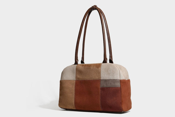 Boxy patchwork suede-look shoulder tote in tan, beige, rust, and brown panels with double brown straps and hanging doll