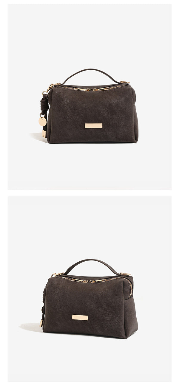 Compact boxy mini handbag with matte pebbled finish, dual top zipper, short top handle, side tassel charm, and gold-tone
