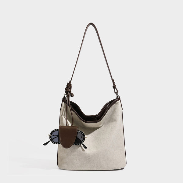Cremefarbene Canvas-Beuteltasche mit dunkelbraunem Besatz in Lederoptik, geknotetem Riemen und befestigter Mini-Tasche, Vorderansicht