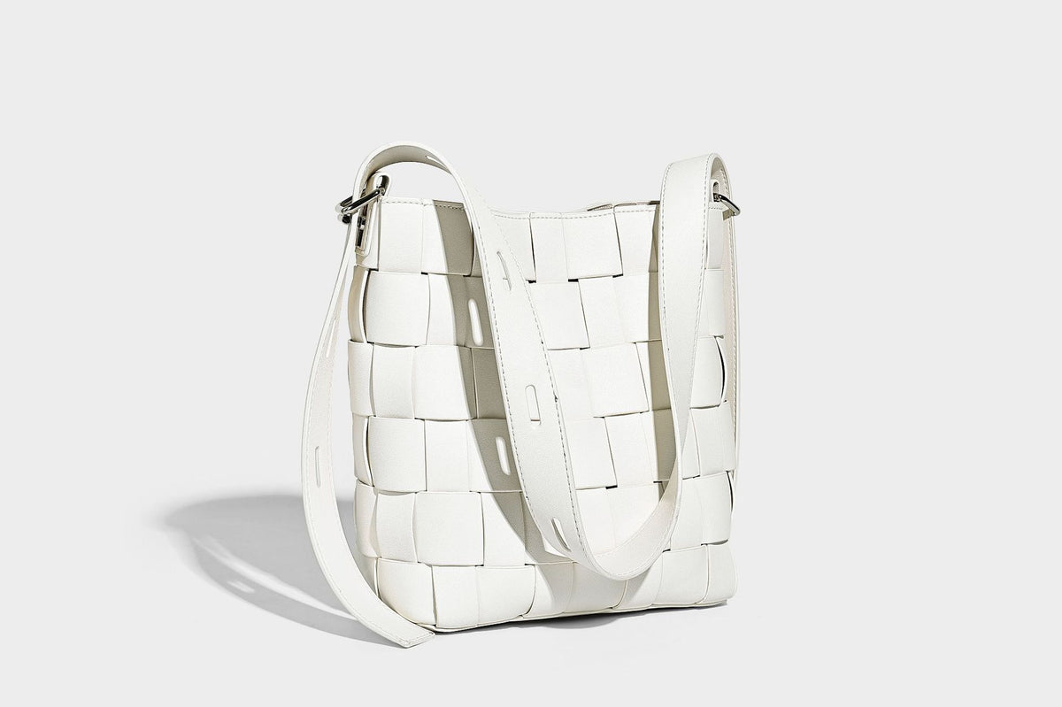 Hand-woven black-and-white checkerboard bucket bag with smooth black trim, silver-tone ring hardware, and adjustable