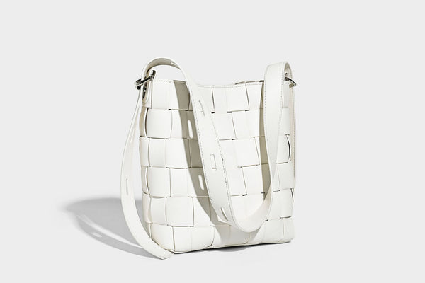 Hand-woven black-and-white checkerboard bucket bag with smooth black trim, silver-tone ring hardware, and adjustable