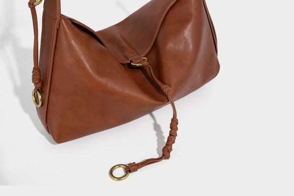 Slouchy brown leather-look shoulder bag with knotted drawcord tie closure, gold-tone ring hardware, and long adjustable