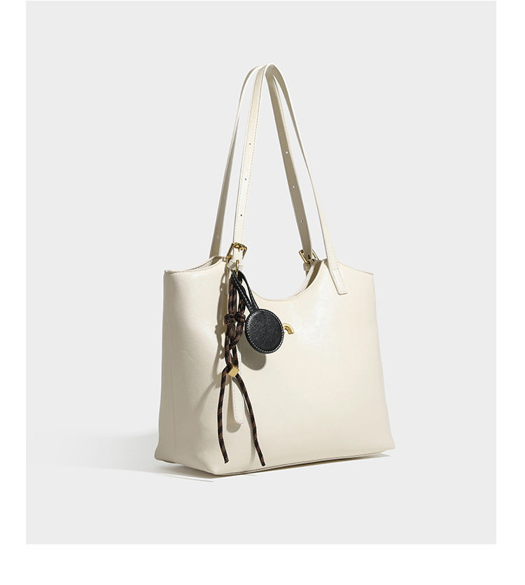 Structured smooth leather-look tote bag with long shoulder strap, gold-tone hardware, and hanging tassel-coin charm, detail