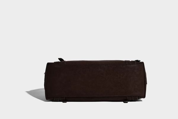 Weiche, zylinderförmige Schultertasche in Dunkelbraun mit silberfarbenen Riemen mit Ösen, Reißverschluss oben, seitlichen Schnallenbeschlägen und Quaste