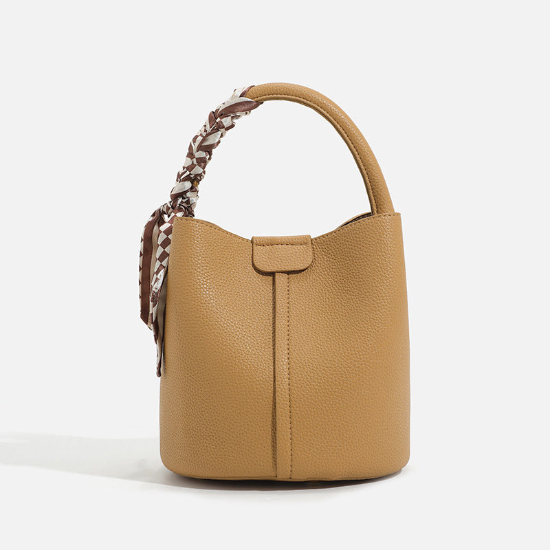 Pebbled leather-look bucket bag with checkered scarf-wrapped top handle, flap tab closure, gold-tone hardware, and matching