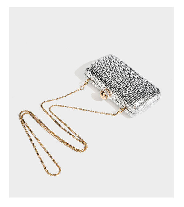 Small structured metallic woven-texture box clutch bag with jeweled kiss-lock dome clasp and slim gold chain strap, detail