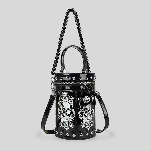 Black glossy cylindrical barrel bag with white skull-floral print panels, silver pyramid studs, black beaded top handle, and