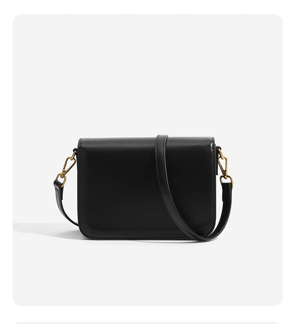 Mini structured black flap crossbody bag with gold-tone ribbed rectangular clasp and adjustable shoulder strap, detail view