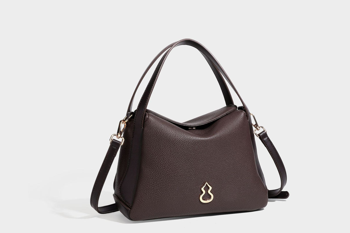 Structured pebbled leather-look shoulder bag with flap top, gold-tone emblem hardware, dual top handles, and detachable