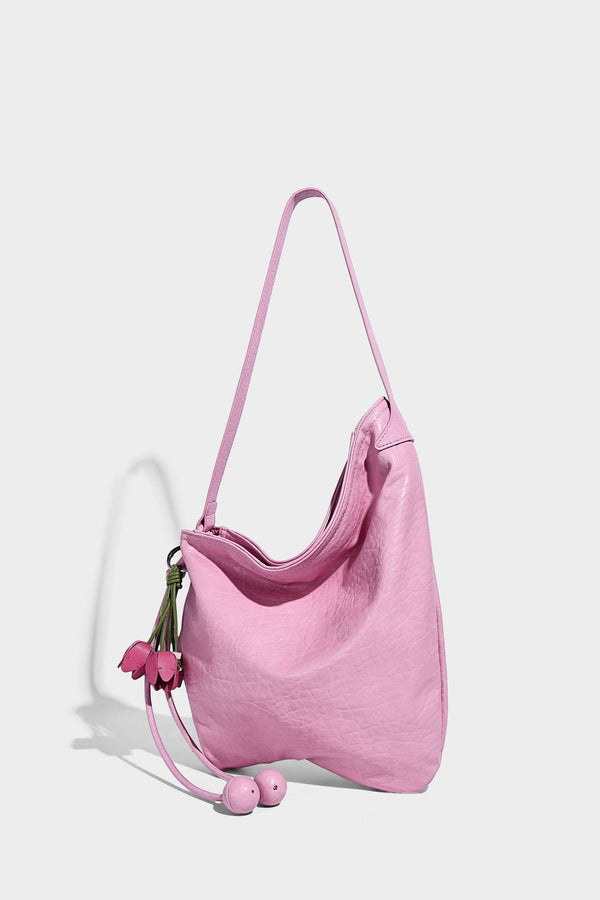 Slouchy hobo shoulder bag in pale yellow with slim strap, drawstring bead closure, and pink tulip floral charm, detail view