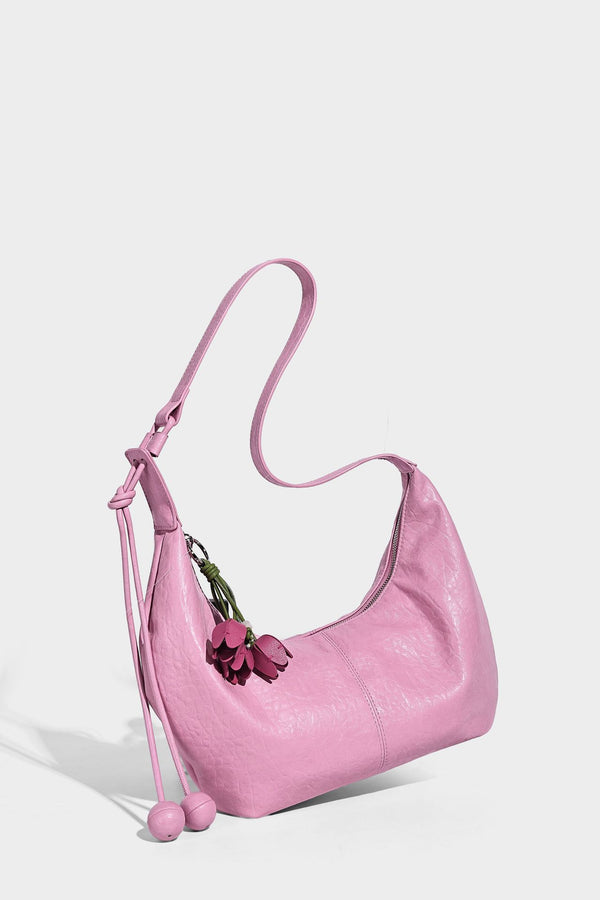 Slouchy crescent half-moon shoulder bag in pink pebbled textured finish with floral charm and knotted side detail, detail