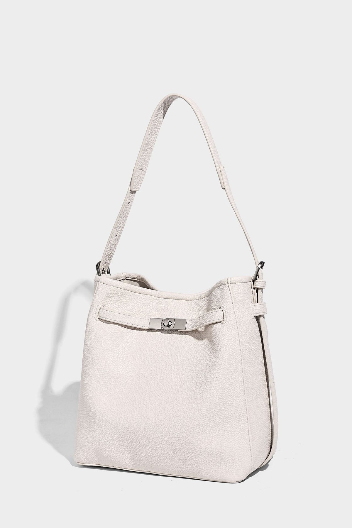 Soft-structured pebbled bucket shoulder bag with front turn-lock strap detail, adjustable strap, and hanging floral tassel