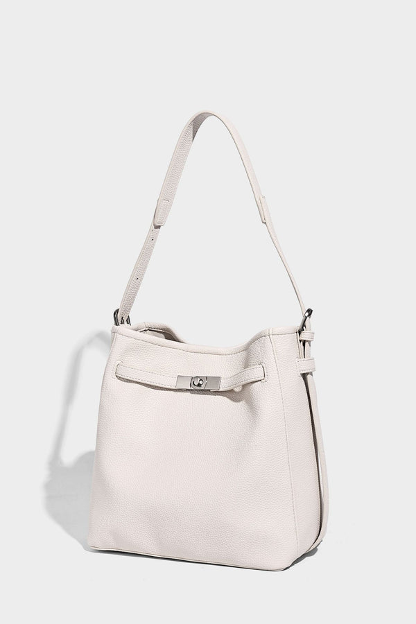 Soft-structured pebbled bucket shoulder bag with front turn-lock strap detail, adjustable strap, and hanging floral tassel