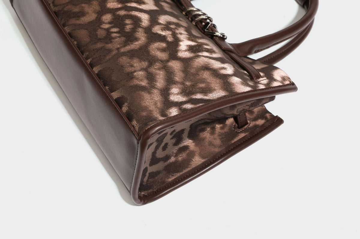 Structured leopard-print tote bag with glossy satin-like finish, dual rounded top handles, silver buckle-and-ring front